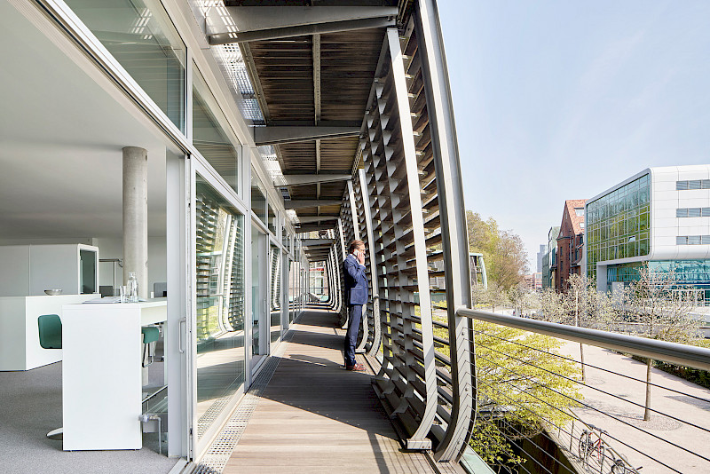 Das Büro verbindet das Innen und Außen mit einem großen Balkon. An einer Kinnarps Bench mit Neo Barhockern von Materia genießt das Team den Blick auf die Elbe.